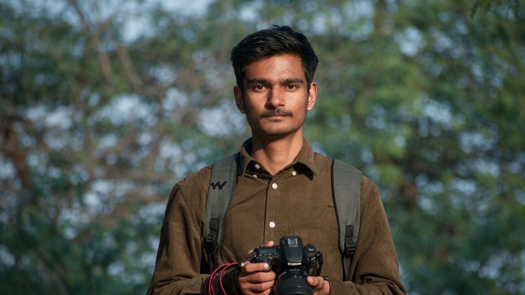 Jovem fotógrafo segurando uma câmera DSLR profissional ao ar livre